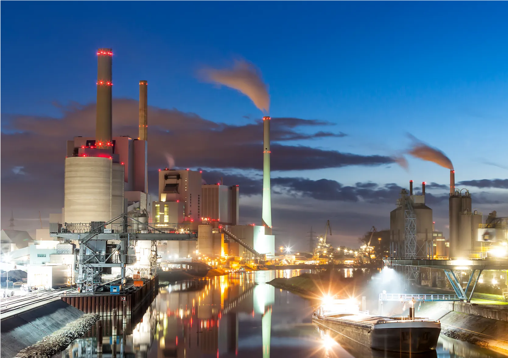 Night view of industrial power plant with chimneys, lights and water reflections in canal