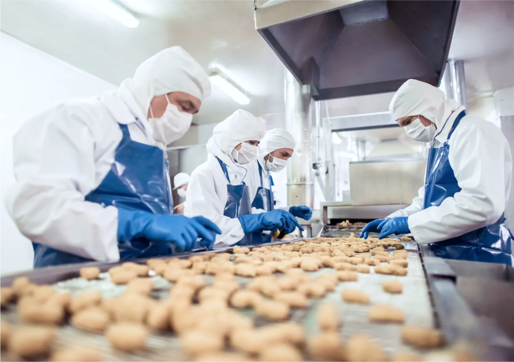 Operators in food processing plant wearing protective clothing and working on frozen product conveyor line